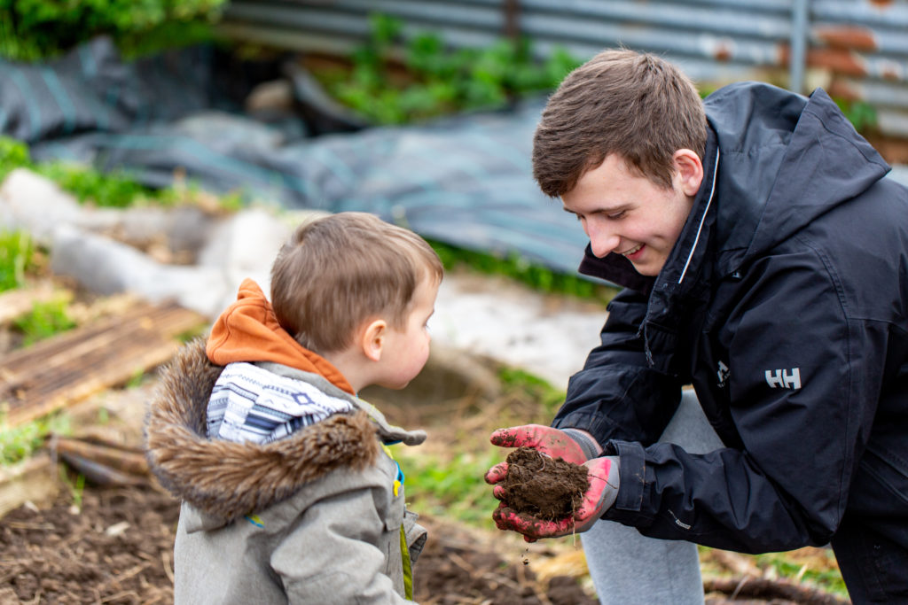 The young man shows the little boy the soil he is holding