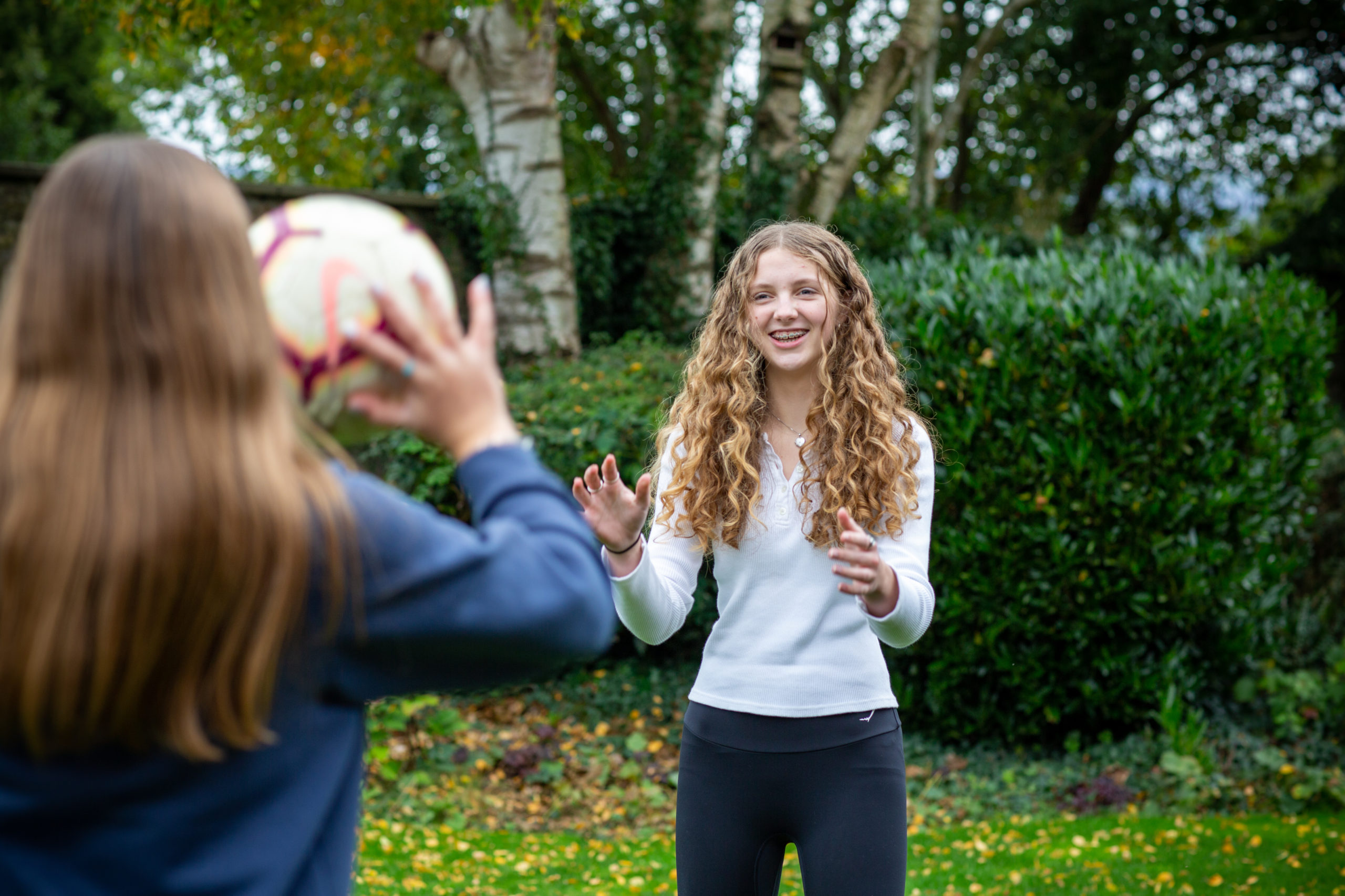 Two teenage girls in the garden, one about to throw a ball to the other